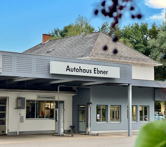 Das Äußere eines Volkswagen-Servicecenters mit einem Schild, das 'Autohaus Ebner' lautet. Ein Auto ist draußen geparkt.
