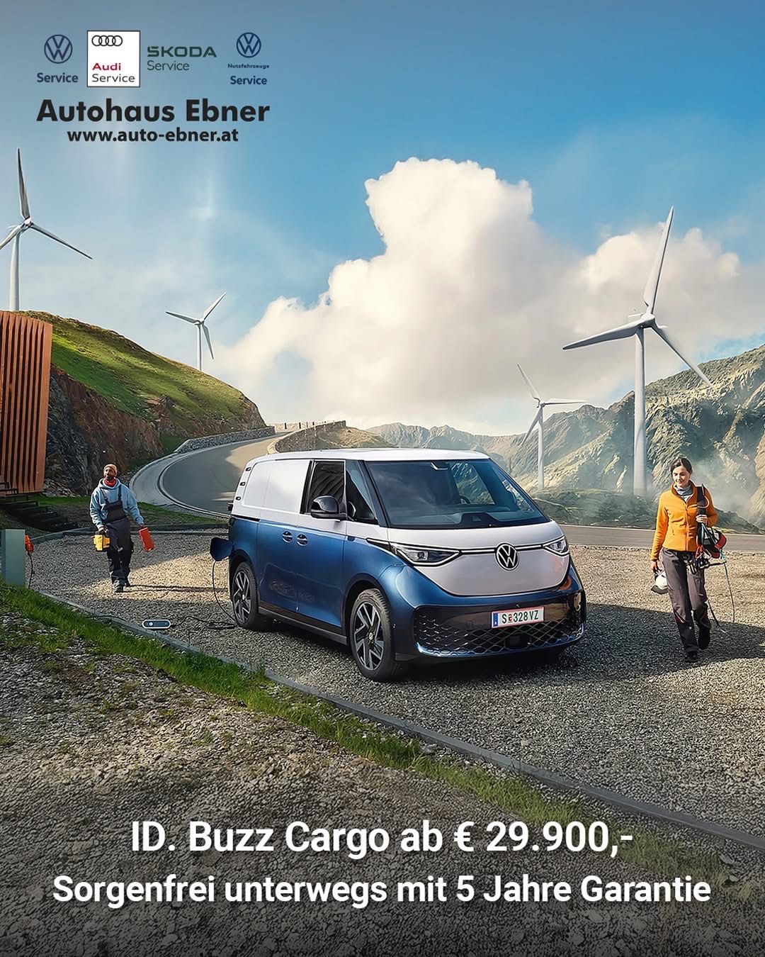 Ein blau-weißer elektrischer VW-Transporter ist auf einer Kiesstraße geparkt, an der zwei Personen vorbeigehen. Dahinter steht eine Windkraftanlage und ein Schild für Autohaus Ebner.