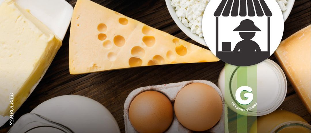 Ein Holztisch mit verschiedenen Lebensmitteln: ein Stück Käse, Eier in einer Schachtel, eine Schüssel mit weißem Reis und ein Logo für City Center Gussing.