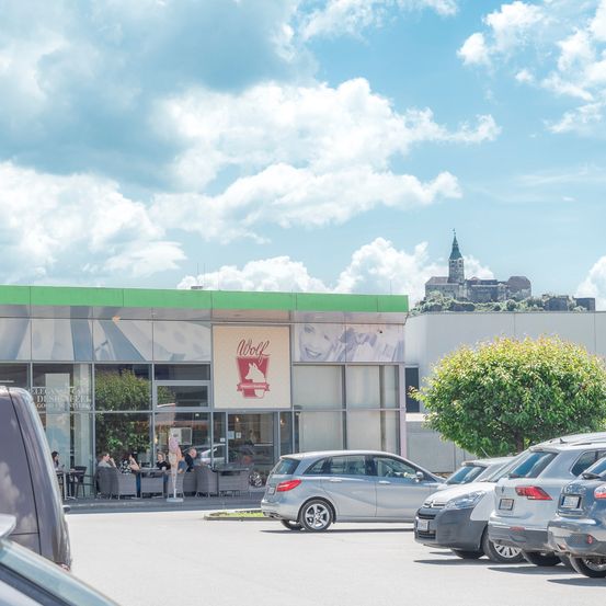 Ein Blick auf das Wolf Restaurant mit einem großen Schild draußen, einigen Leuten, die an Tischen sitzen, und einer schönen Burg im Hintergrund.