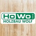 Ein Logo für Holzbau Wolf GmbH auf einer Holzoberfläche. Das Logo zeigt den Firmennamen in grünen Buchstaben auf weißem Hintergrund mit einem grünen Rand. Der Text ist in einer fetten, serifenlosen Schrift geschrieben.