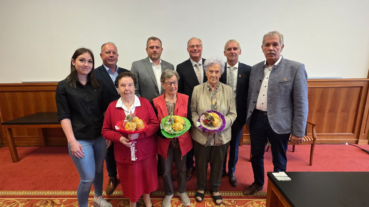 Mehrere Menschen in formeller Kleidung stehen für ein Gruppenfoto. Die Frauen halten Körbe mit Obst.