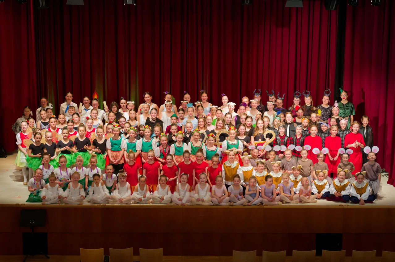 Eine Gruppe von Kindern in verschiedenen Kostümen, wahrscheinlich für eine Aufführung, posiert für ein Foto auf der Bühne.