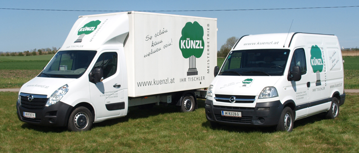 Zwei weiße Lieferwagen mit grünen Logos stehen auf einer Wiese. Der linke Van hat ein Baumlogo, der rechte ein Säulenlogo. Beide haben 'KUNZL' auf der Seite geschrieben.