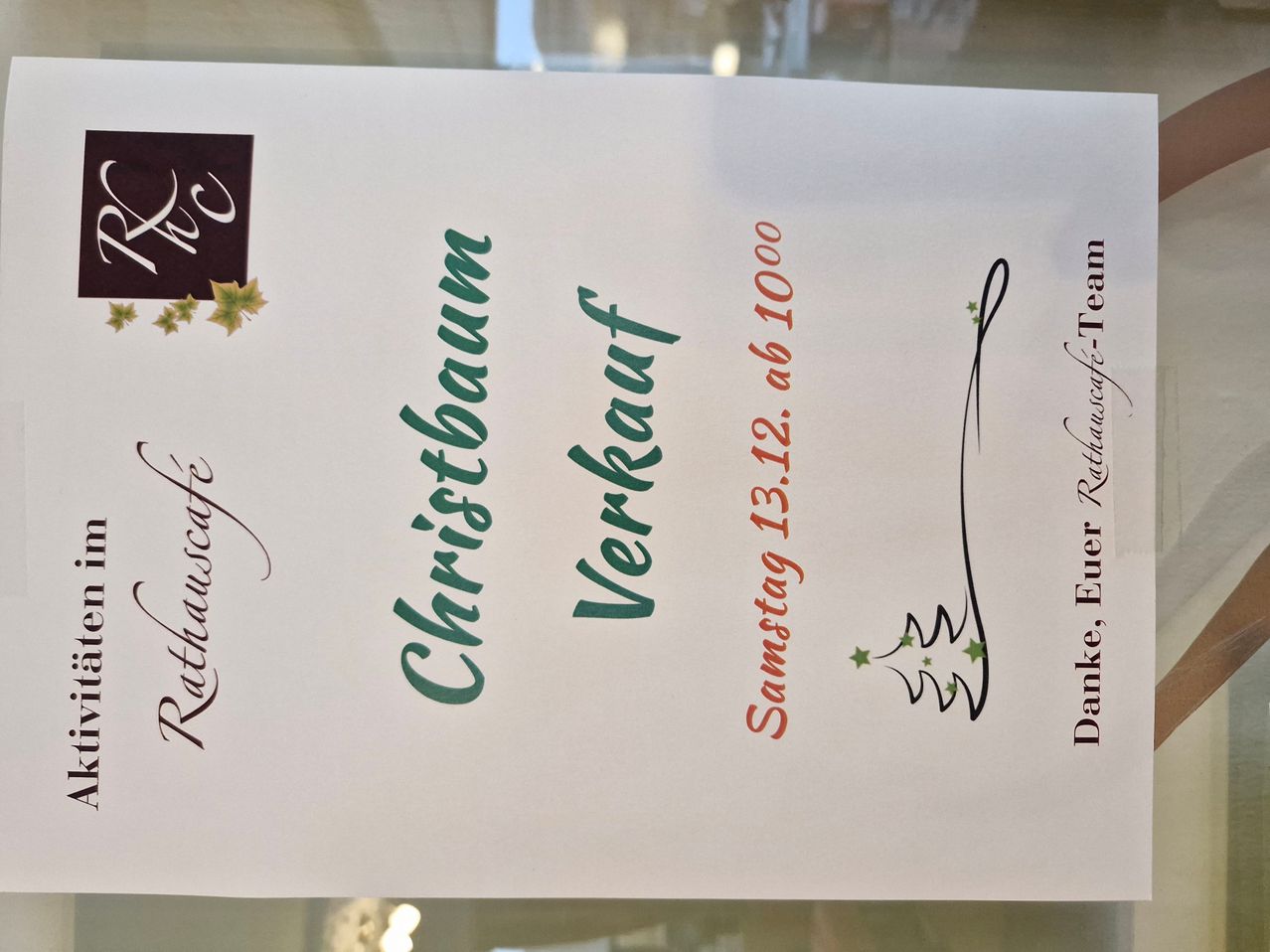 Ein weißes Papier mit schwarzem Rand enthält Text in verschiedenen Farben. 'Weihnachtsbaum' ist in Grün, 'Verkauf' in Orange und 'Samstag 12. ab 12:00 Uhr' in Rot geschrieben. Rechts befindet sich ein Logo.