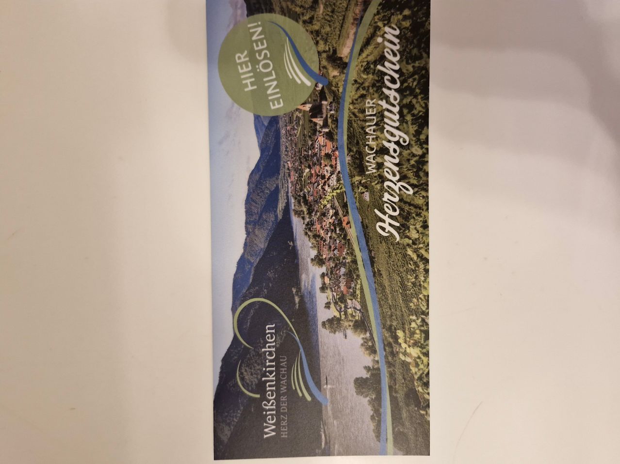 Poster für Weinsenkkirchen Herz der Wachau mit einer malerischen Aussicht auf Berge und ein Dorf.