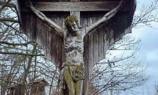 Ein hölzernes Kruzifix von Jesus Christus ist an einem Kreuz befestigt und im Freien in einer ländlichen Umgebung aufgestellt.