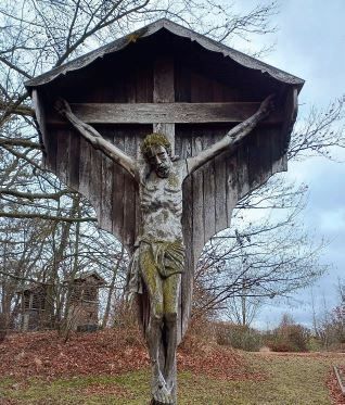 Ein hölzernes Kruzifix von Jesus Christus ist an einem Kreuz befestigt und im Freien in einer ländlichen Umgebung aufgestellt.