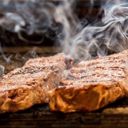 Zwei Steaks werden auf einem Grill gebraten, wobei Rauch austritt. Der Rauch ist weiß und verschwommen.
