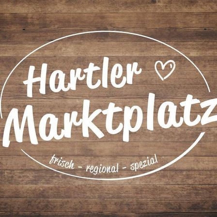 Ein hölzerner Hintergrund mit einem Logo für Hartler Marktplatz, mit Herzsymbol und Text 'frisch - regional - spezial'.