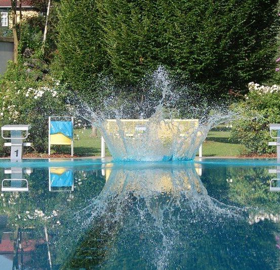 Ein Taucher springt in den Pool mit den Nummern 1 und 3 an der Seite, umgeben von einem üppigen Garten.