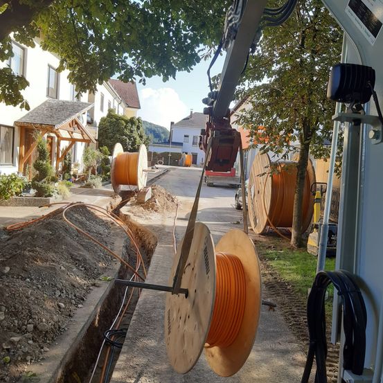 Bauarbeiter verlegen Kabel in einem Wohngebiet. Geräte sind aufgestellt und orangefarbene Kabel werden durch den Boden gezogen.