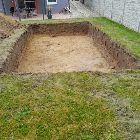 Ein leerer rechteckiger Bereich wird in einem Garten gegraben und von einem Grasfeld umgeben.