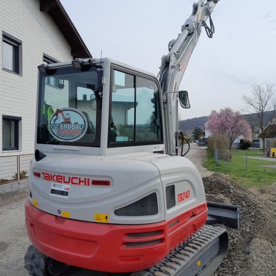 Ein roter und weißer Takeuchi-Minibagger steht vor einem Haus mit Ziegelwänden.