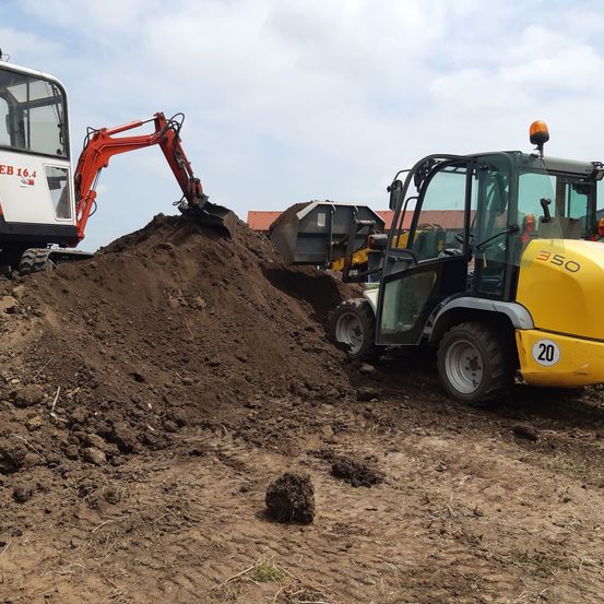 Zwei Baufahrzeuge arbeiten auf einer Erdbaustelle. Ein roter Bagger schaufelt Erde auf, während ein gelber Bulldozer mit der Nummer 20 in der Nähe geparkt ist.