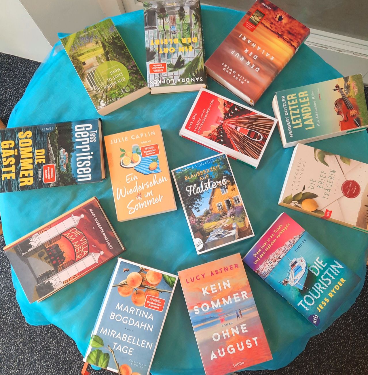 A collection of books arranged on a blue cloth, including titles like 'Die Villa Am Meer' and 'Kein Sommer Ohne August'.'