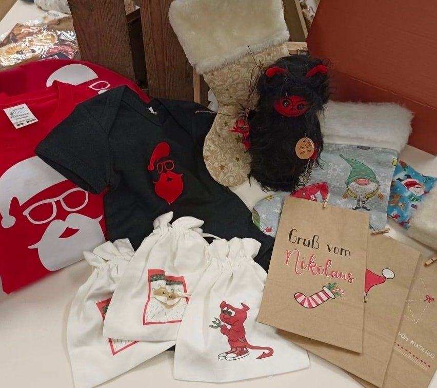 Auf einem Tisch sind verschiedene Weihnachtsartikel zu sehen, darunter ein Santa-Claus-Outfit, eine rote Teufelspuppe und verschiedene Geschenktüten mit festlichen Aufdrucken.