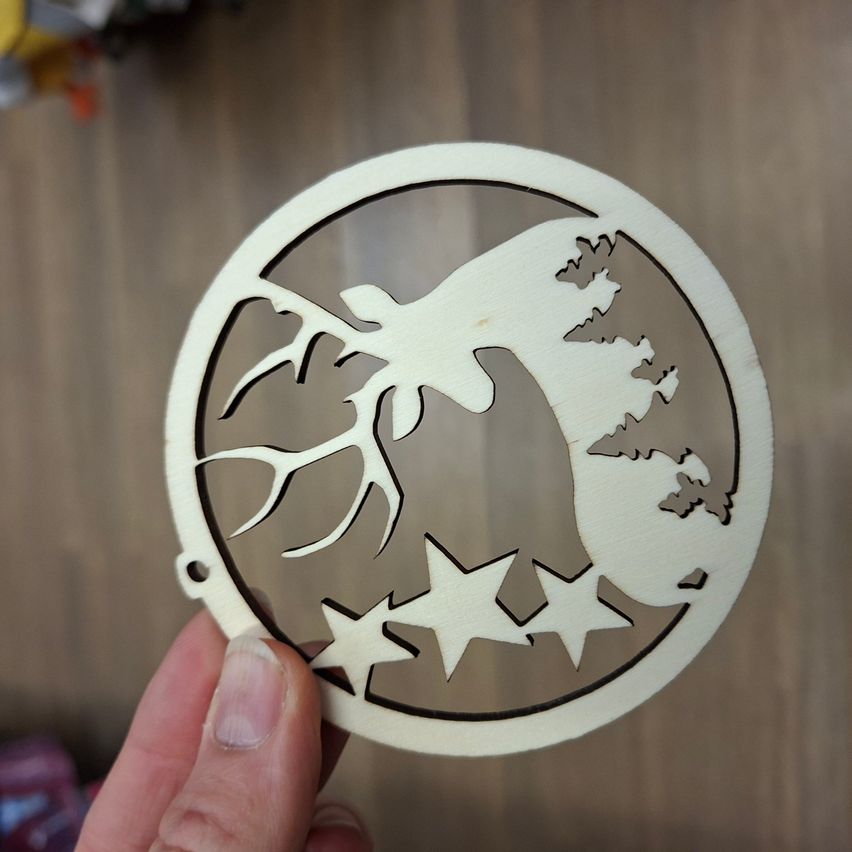 Ein hölzerner Weihnachtsschmuck in Form eines Hirsches mit Sternen, gehalten von einer Person auf einer hölzernen Oberfläche.