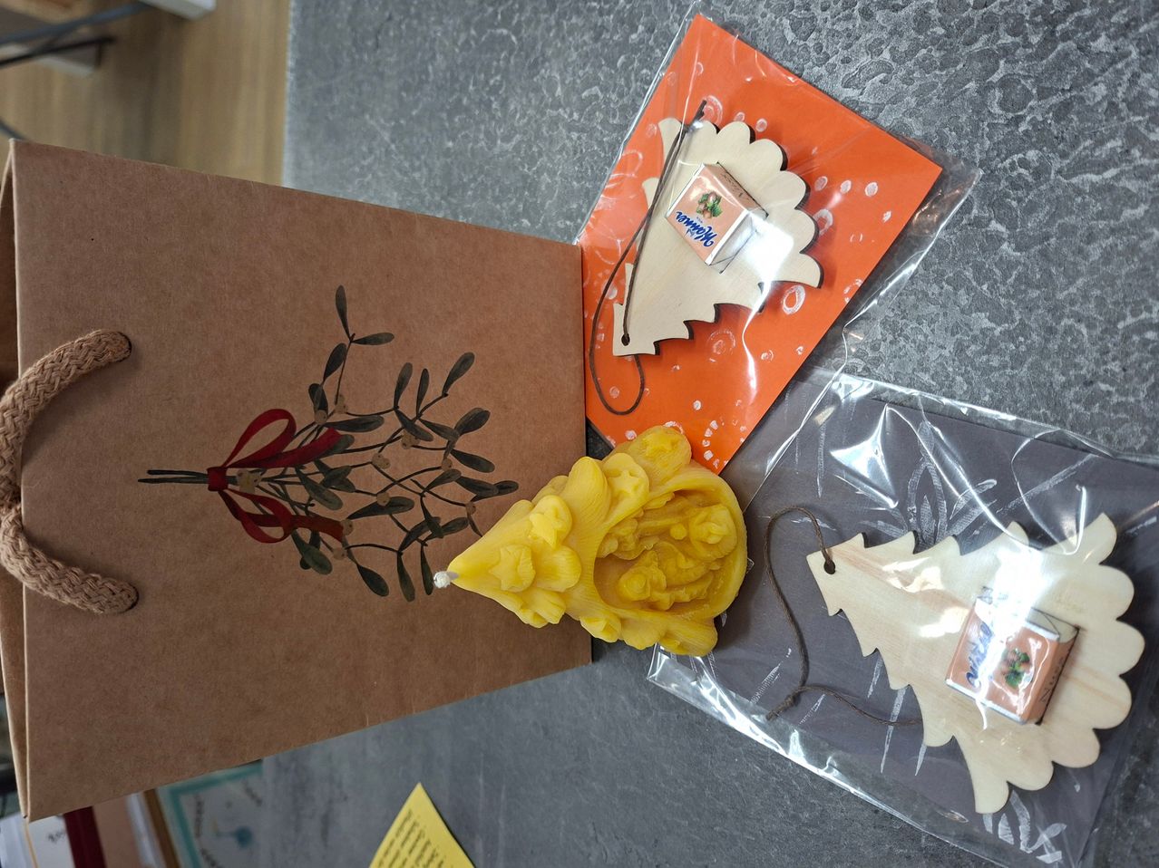 Ein brauner Papierbeutel mit einer Mistelzeichnung, einer gelben Weihnachtsbaumkerze und einer kleinen Box mit dem Wort 'Mints' darauf.