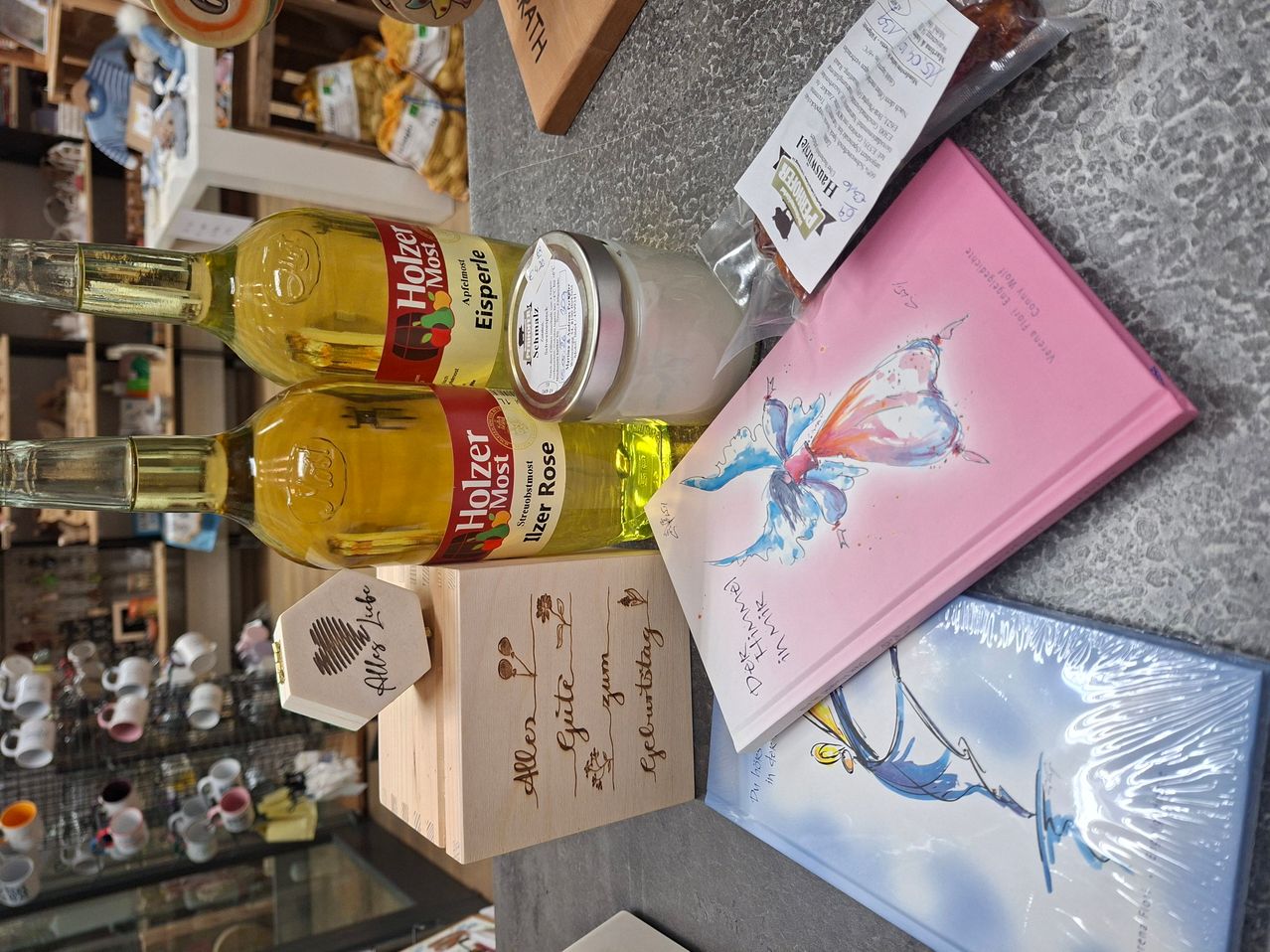Two bottles of Holzer Most are stacked with a small wooden box, a glass jar, and two books on a countertop.