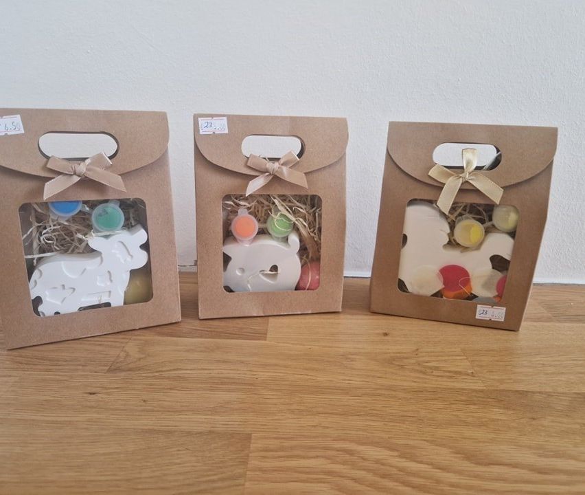 Drei braune Papiertüten mit Bändern auf einer Holzoberfläche. Jeder Beutel enthält verschiedene bunte Babyspielzeuge. Der erste Beutel hat ein schafförmiges Spielzeug, der zweite hat ein herzförmiges Spielzeug und der dritte hat eine Mischung aus Spielzeugen.