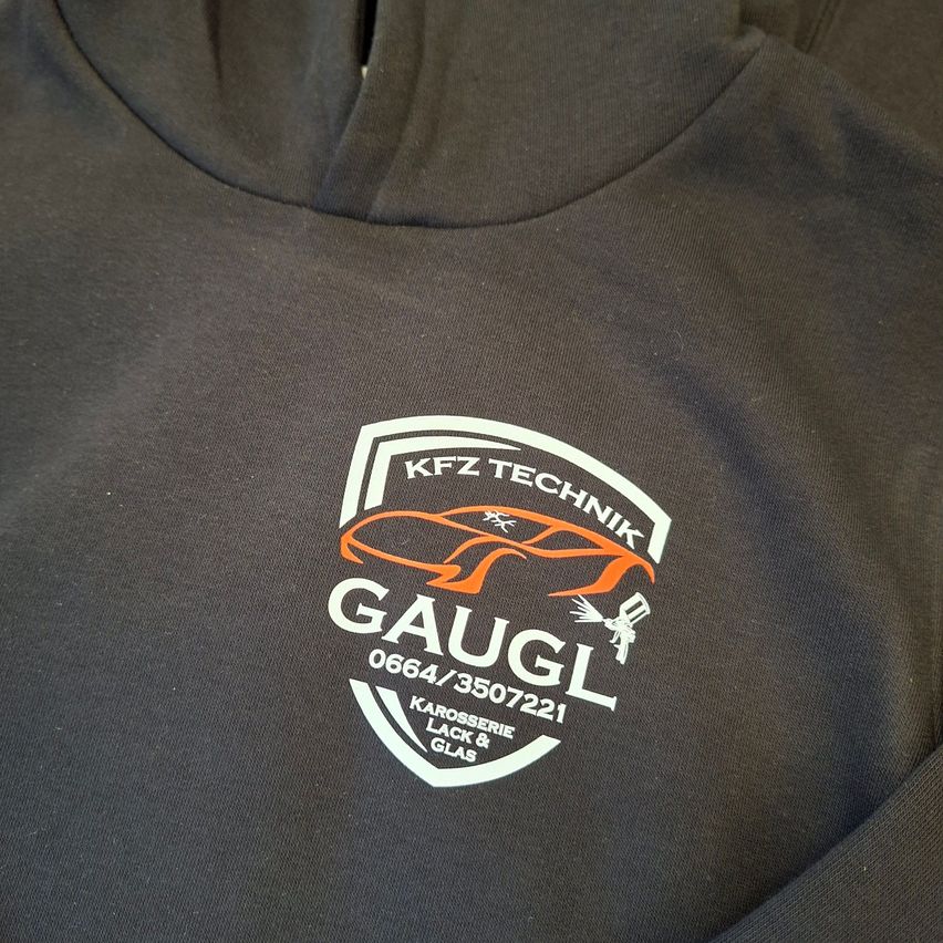 Ein schwarzes Sweatshirt mit einem weißen Logo, das ein Auto und den Text 'KFZ TECHNIK GAUGL 0664/3507221 Karosserie Lack & Glas' zeigt.