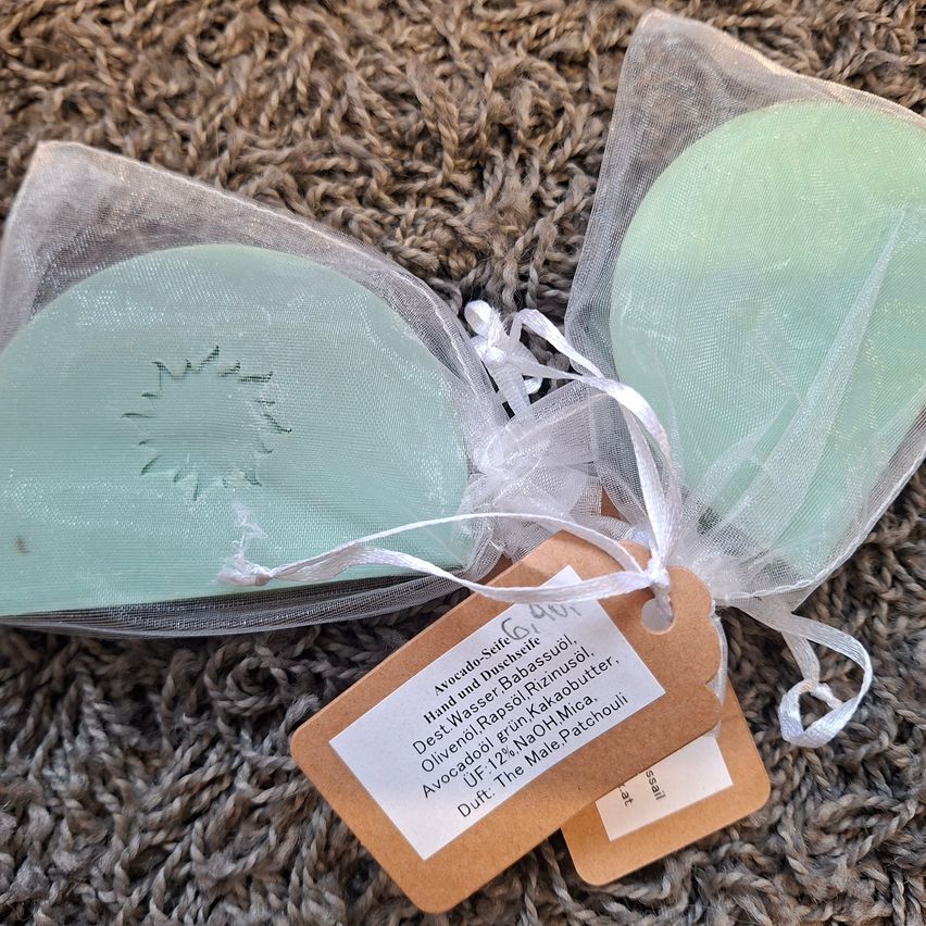 Two green soaps in clear plastic bags with a brown tag, one with a sun design, on a brown carpet.