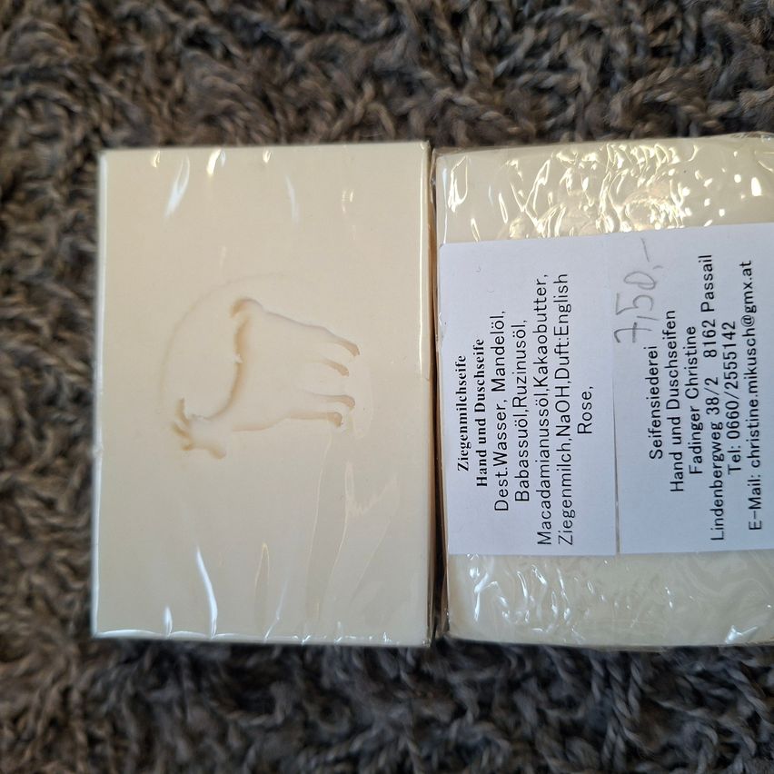 Two soaps with a label displaying 'Ziegenmilchseife Hand und Duschseife' and a faint imprint of a goat on the left soap. The label also includes ingredients and contact information.