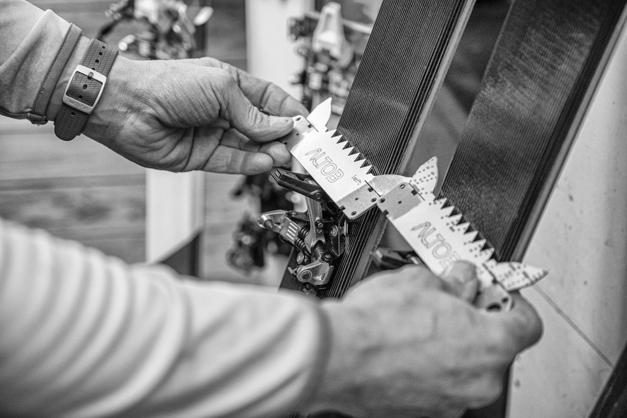 A person is using a measuring tool on a metal object, possibly a snowboard. The tool has 'ALTOB' on it.