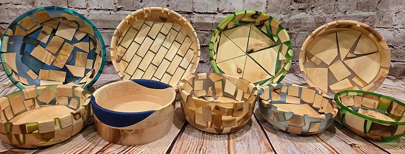 Eine Reihe von Holzschalen mit einzigartigen Mosaikdesigns, die auf einer Holzoberfläche vor einer Ziegelwand ausgestellt sind.