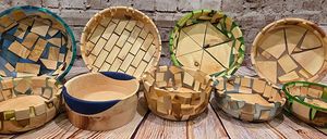 Eine Reihe von Holzschalen mit einzigartigen Mosaikdesigns, die auf einer Holzoberfläche vor einer Ziegelwand ausgestellt sind.