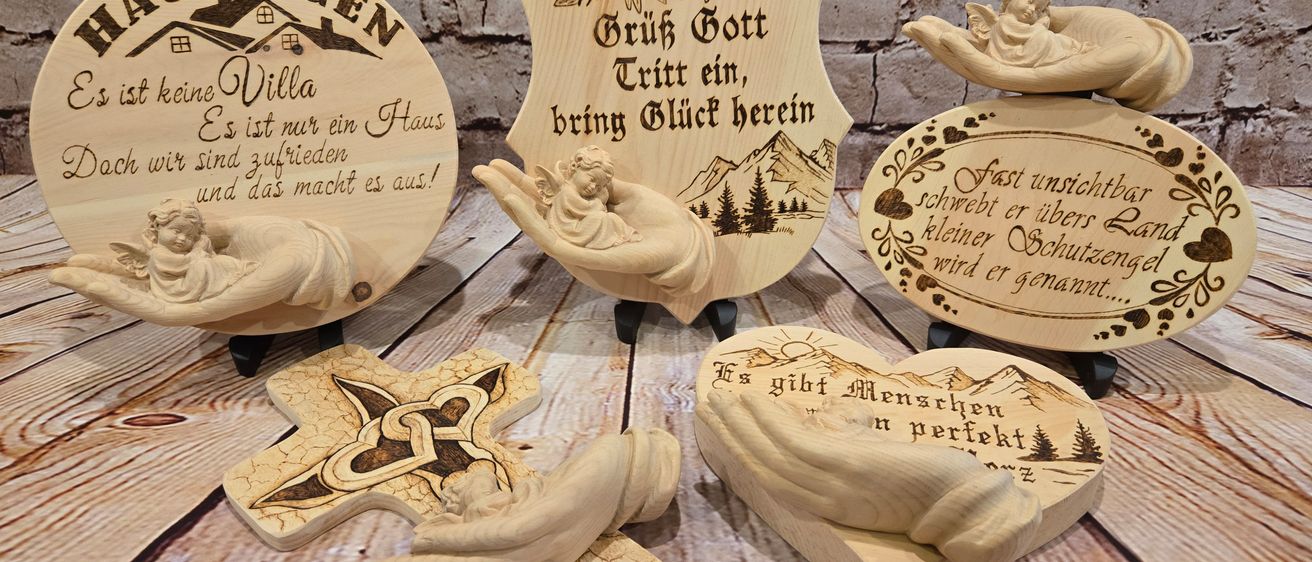 Vier Holzobjekte liegen auf einer Holzoberfläche. Jedes ist kunstvoll mit verschiedenen Designs und Texten geschnitzt. Eines lautet 'Es ist nur ein Haus,' ein anderes 'Gute Nacht,' ein drittes 'Gib ein, bring Glück,' und das letzte hat ein Kreuzdesign.
