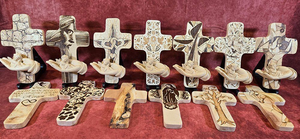 Eine Sammlung handgeschnitzter Holzkreuze auf rotem Hintergrund, jedes mit einzigartigen Designs und Engelfiguren.