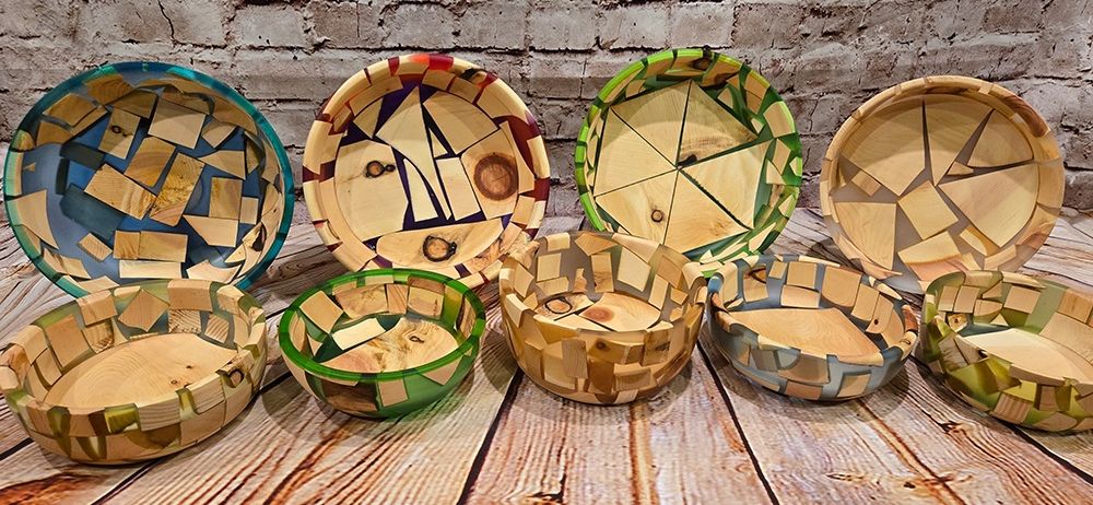 Auf einem Holztisch ist eine Auswahl handgefertigter Holzschüsseln zu sehen, jede einzigartig mit einer Mosaik aus verschiedenfarbigen Holzstücken gestaltet.