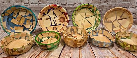 Auf einem Holztisch ist eine Auswahl handgefertigter Holzschüsseln zu sehen, jede einzigartig mit einer Mosaik aus verschiedenfarbigen Holzstücken gestaltet.