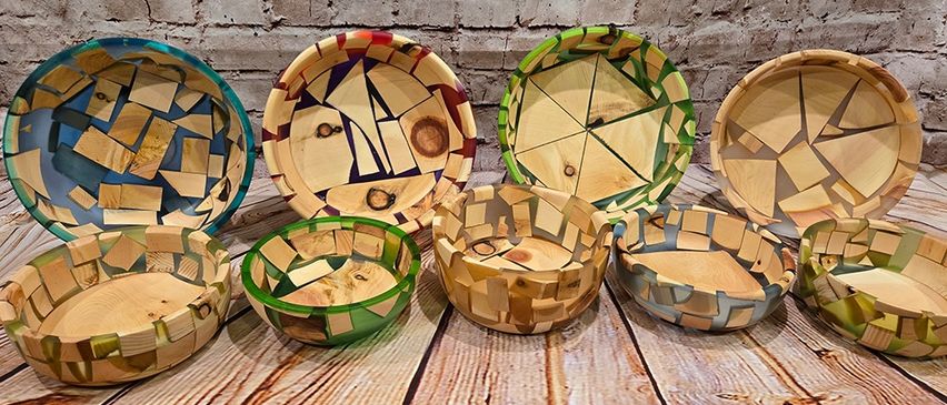 Auf einem Holztisch ist eine Auswahl handgefertigter Holzschüsseln zu sehen, jede einzigartig mit einer Mosaik aus verschiedenfarbigen Holzstücken gestaltet.