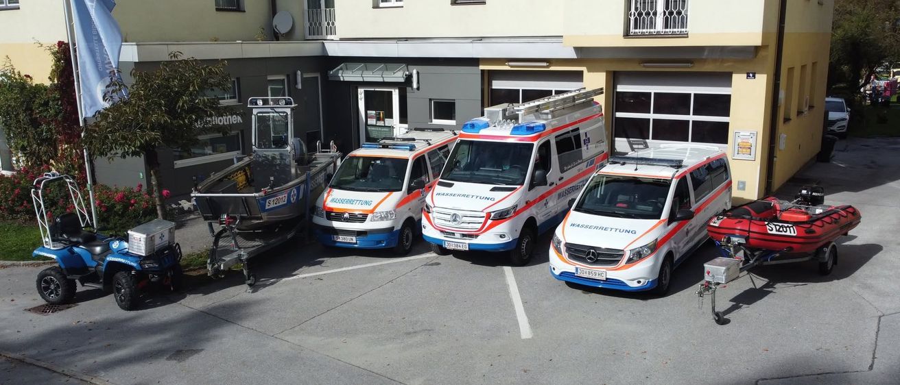 Drei Krankenwagen und ein Boot sind vor einem Gebäude mit mehreren Fenstern und einem Balkon geparkt.