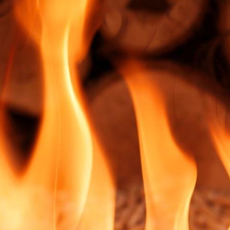 Eine Nahaufnahme eines Feuers mit brennendem Holz, das orange und gelbe Flammen und ein leuchtendes, warmes Licht erzeugt.