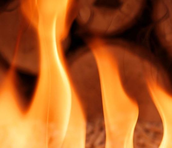 Eine Nahaufnahme eines Feuers mit brennendem Holz, das orange und gelbe Flammen und ein leuchtendes, warmes Licht erzeugt.