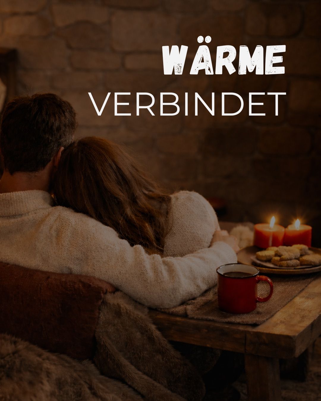 Ein Paar sitzt eng beieinander und genießt einen warmen Moment am Kamin. Sie sehen sich an und halten Händchen. Auf dem Tisch steht eine rote Tasse, Kekse und brennende Kerzen. Der Kamin besteht aus Ziegelsteinen. Die Worte 'Wärme verbindet' sind in Weiß geschrieben.
