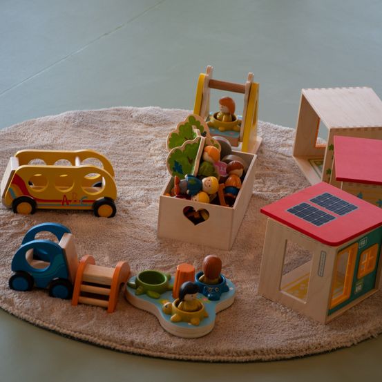 Ein Spielbereich mit verschiedenen Spielzeugen: ein Bus, ein LKW, eine mit Figuren gefüllte Aufbewahrungsbox, ein Haus mit Solarmodulen und einem Teppich.