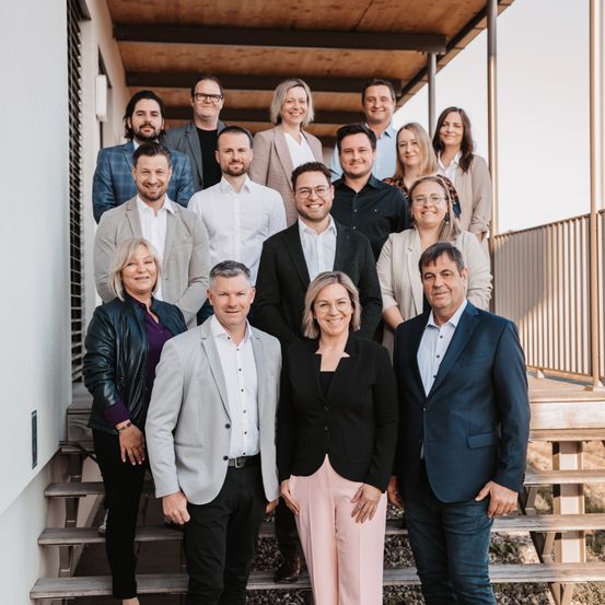 Eine Gruppe von Fachleuten steht auf den Stufen eines modernen Gebäudes und lächelt für ein Foto.