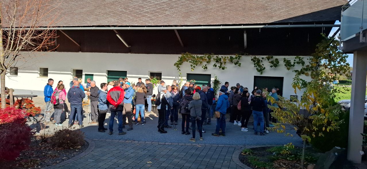 Eine Gruppe von Menschen steht in einer Schlange vor einem Gebäude, einige schauen auf etwas vor ihnen, einige tragen Hüte und Schuhe.