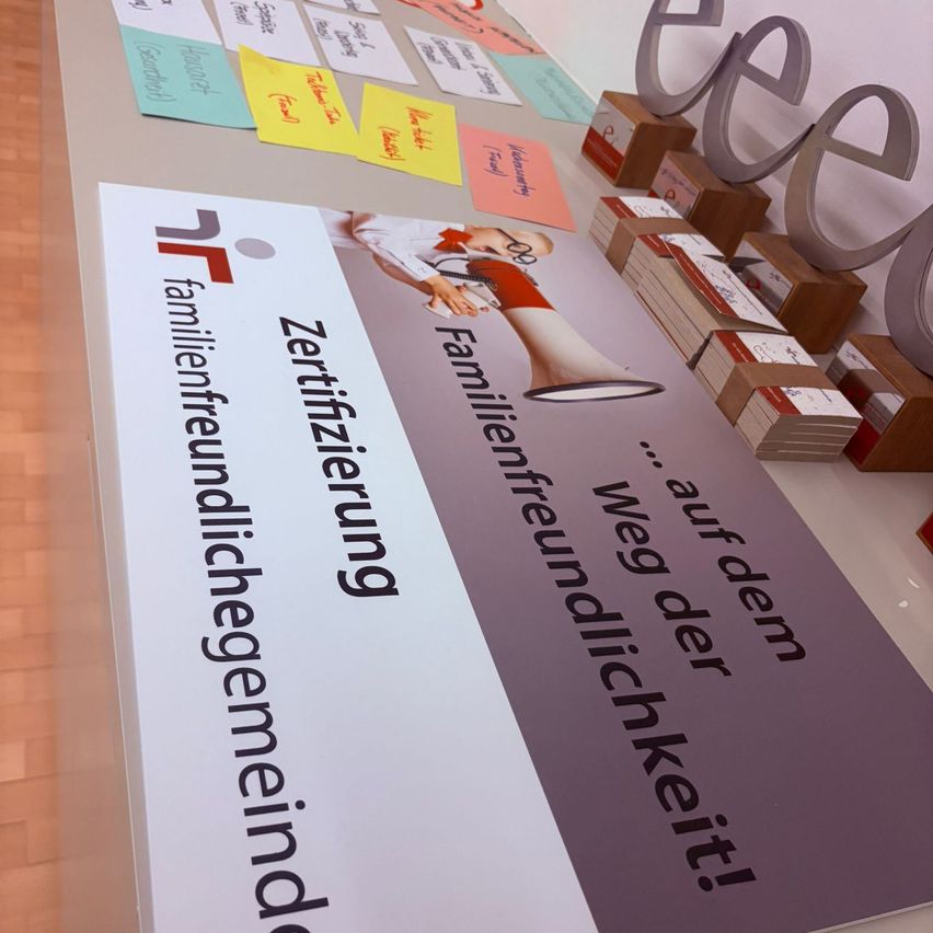 A display board with the text 'family-friendly certificate' and a megaphone illustration sits on a table with several colorful sticky notes and boxes.