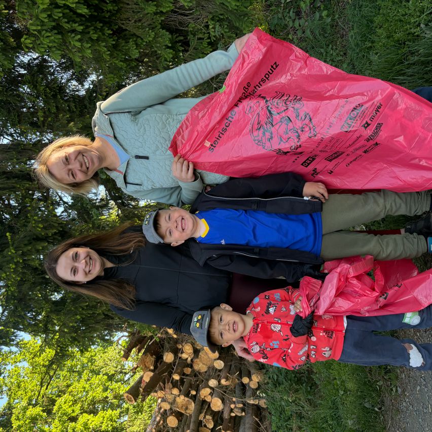 Four people smile for the camera. Two women and two boys. They hold plastic bags. The background shows trees and logs.