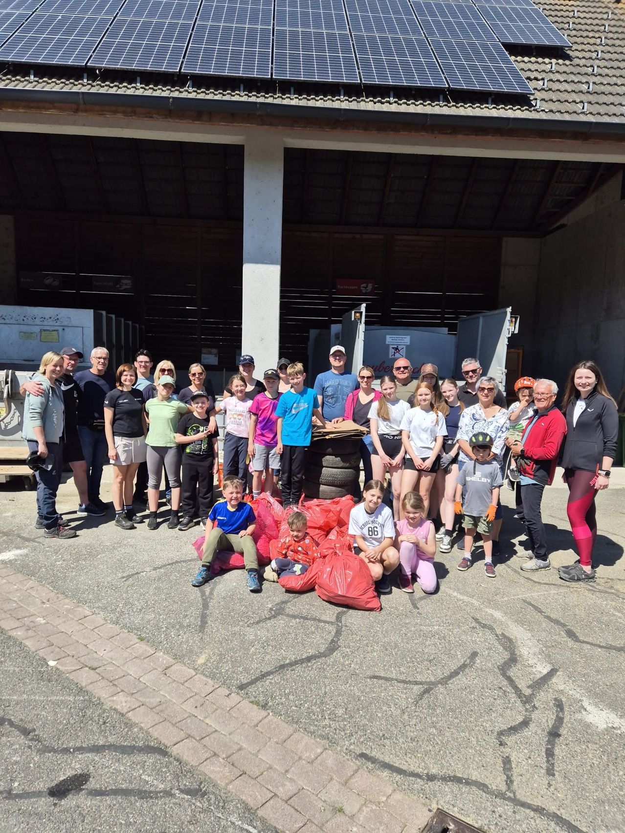 A group of people, including children, pose for a photo in front of a building with bags of trash.