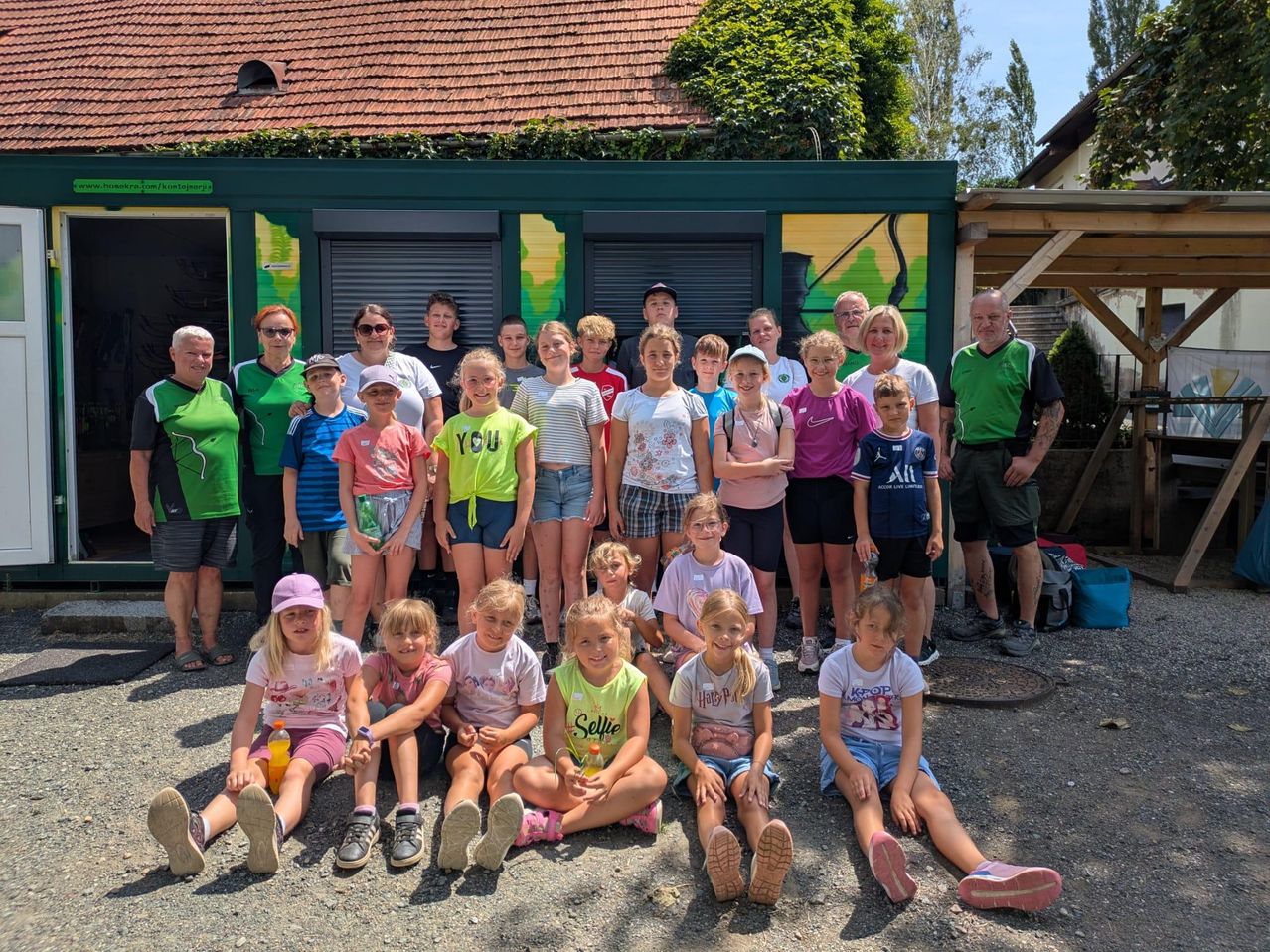 Gruppe von Kindern und Erwachsenen vor einem grünen Container mit bemalter Fassade
