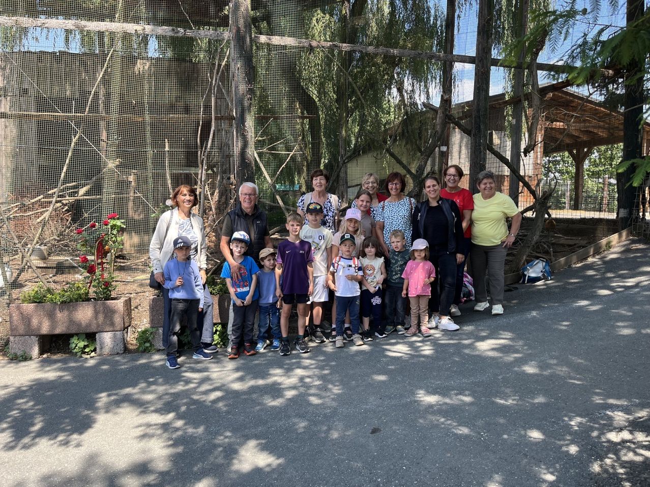 Gruppe von Erwachsenen und Kindern steht vor einem Vogelgehege in einem Zoo.