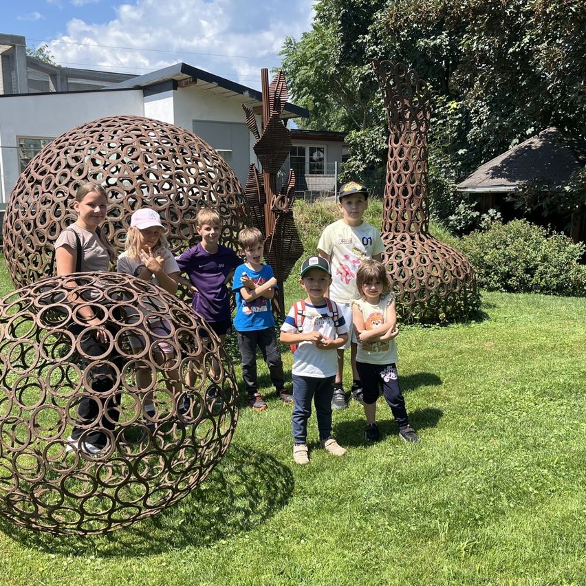 Eine Gruppe von Kindern und Erwachsenen posiert für ein Foto vor großen Metallskulpturen in einem Park.