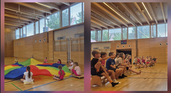 Kinder spielen mit einem bunten Fallschirm in einer Turnhalle, einige sitzen auf dem Boden und andere auf einer Bank.